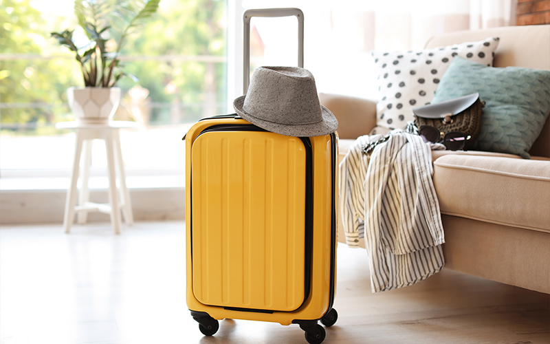 Prise de possession rapide Une valise jaune à roulettes avec un chapeau sur le dessus, placée près d’un fauteuil.